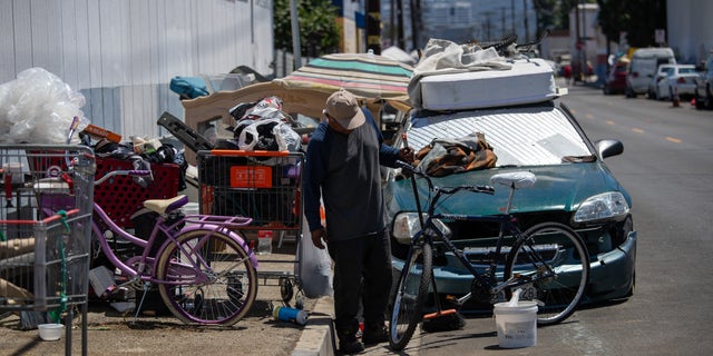 A homeless man sweeps up around a sidewalk encampment on Deering Avenue on July 10, 2023 in Canoga Park, California.