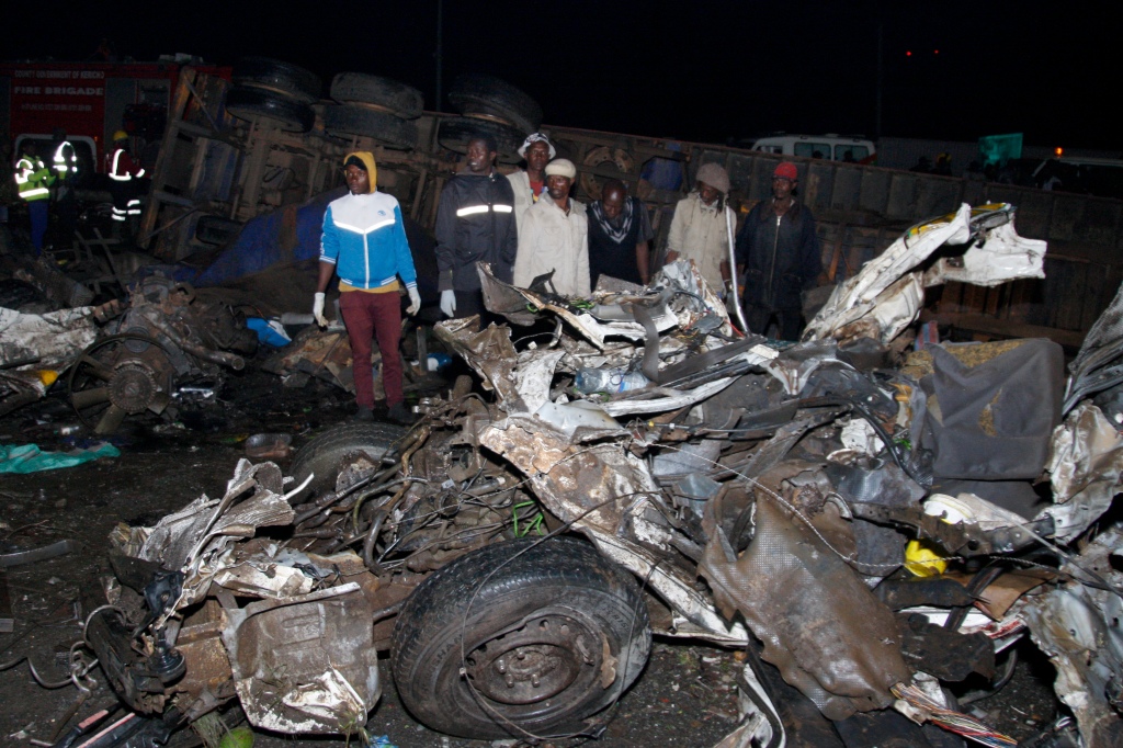 People stand near the wreckage of vehicles after the fatal accident in Londiani, Kenya on July 1, 2023. 