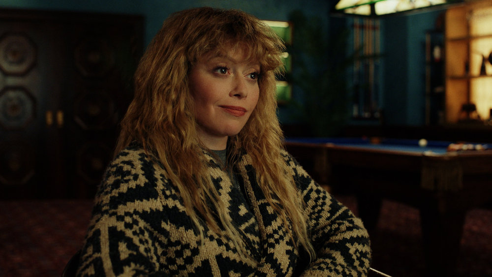 Natasha Lyonne in "Poker Face." She's wearing a gold-and-black sweater. Her hair is long and she's got a smirk on her face and she looks off-camera.