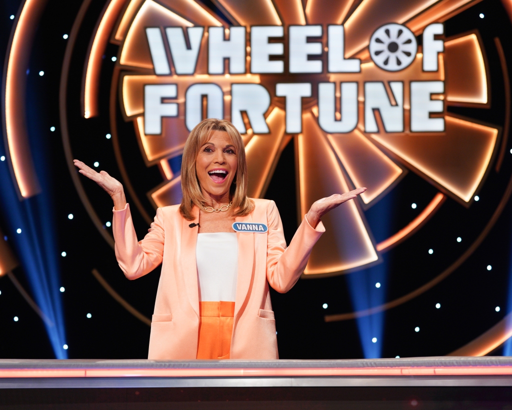 Vanna White on Wheel of Fortune with show name behind her. 