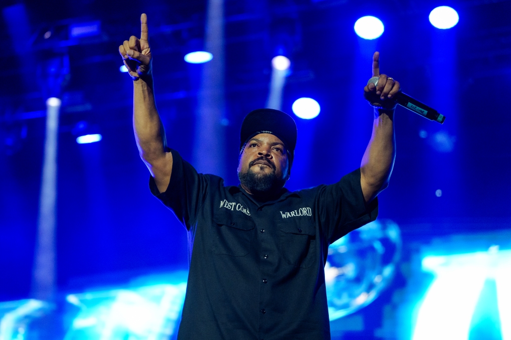 Ice Cube onstage holding a mic with his hands in the air. 