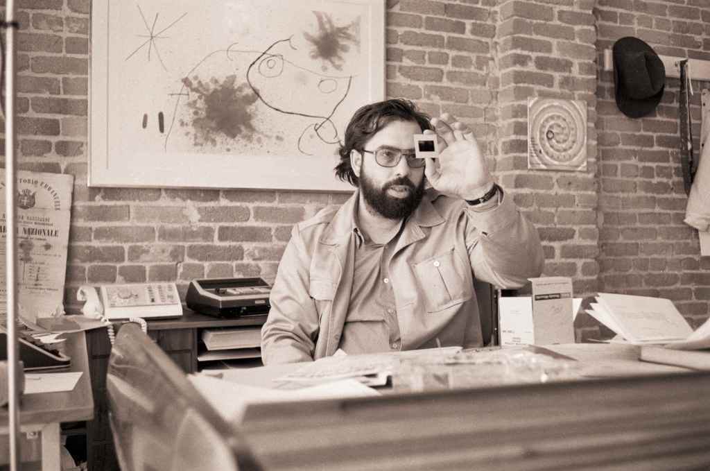 Francis Ford Coppola seated at a desk and looking at a film slide