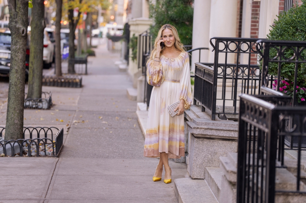 Carrie Bradshaw walks down the street in a flowy dress while on the phone with a friend.