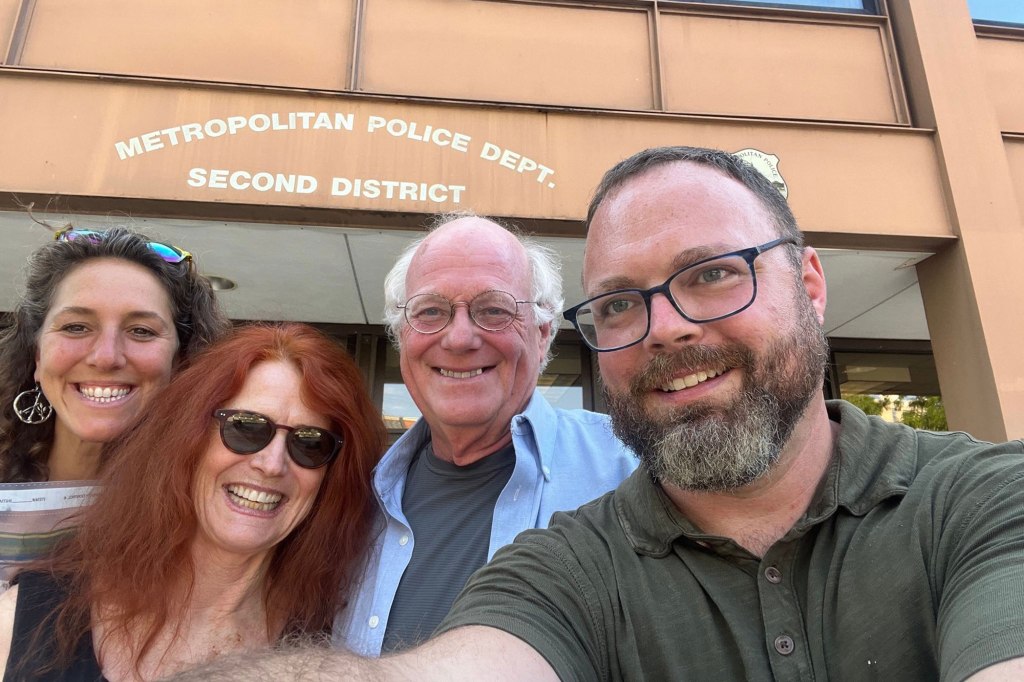 Ben Cohen, Jodie Evans and other supporters smile in a selfie in front of the Metropolitan Police Dept. building. 