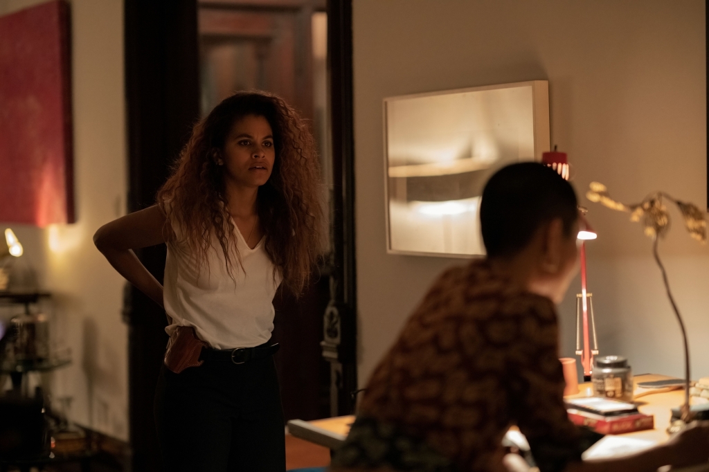 Zazie Beetz standing in a room looking at a woman at a desk. 