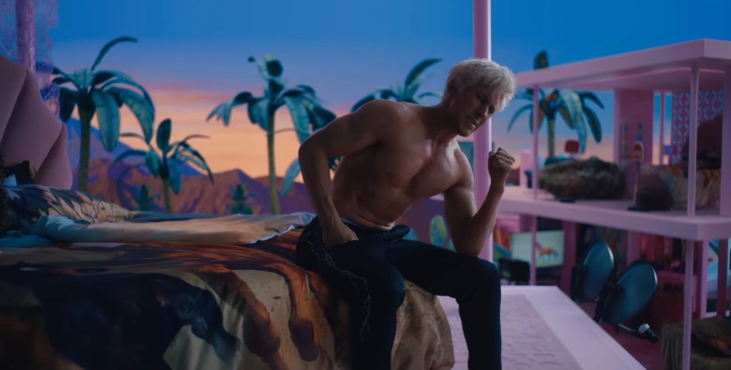 Ryan Gosling sits on a bed, shirtless, while singing his song "I'm Just Ken."