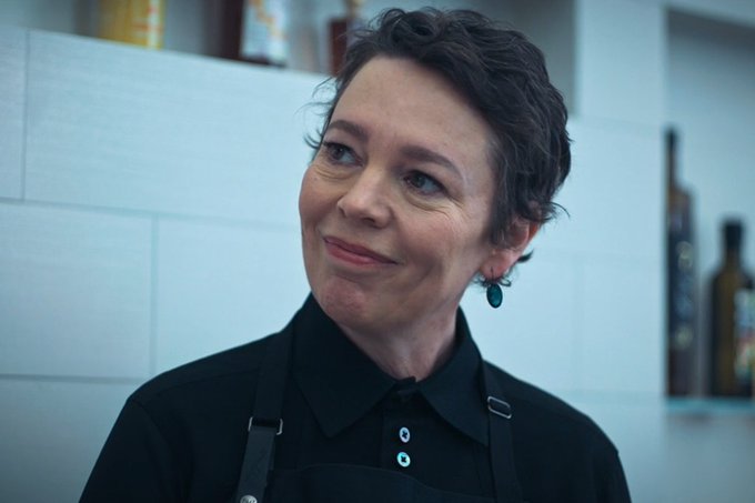 Olivia Colman smiles in a chef's uniform.
