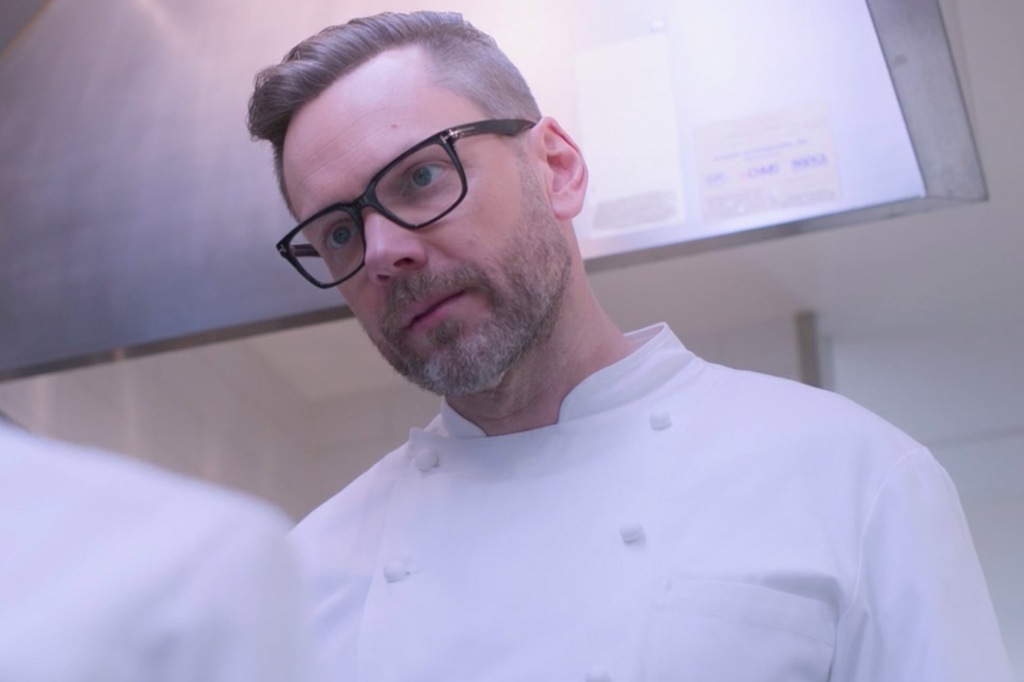 Joel McHale towers over an off-screen character while wearing a chef's uniform.