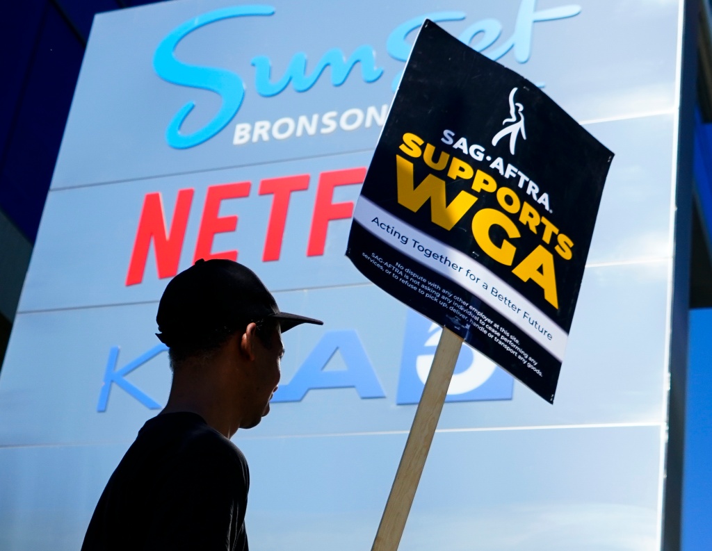 WGA striker in front of streaming service signs