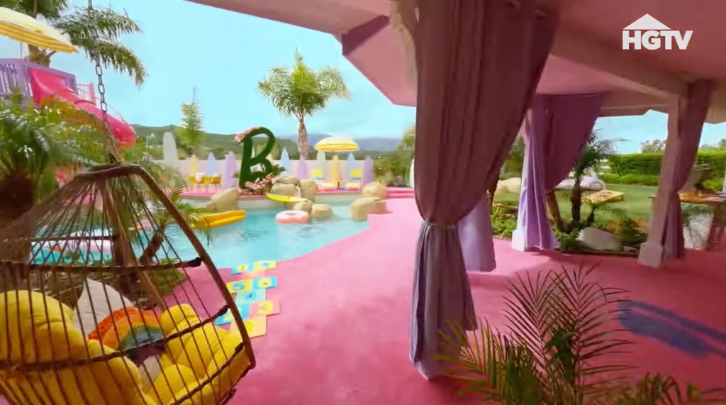 A pool area behind a house, with pink furniture. 