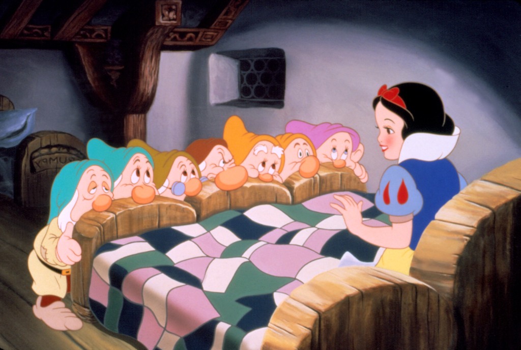 An image from Disney's "Snow White and the Seven Dwarves" animated feature shows Snow White in bed with the seven dwarves looking up at her.