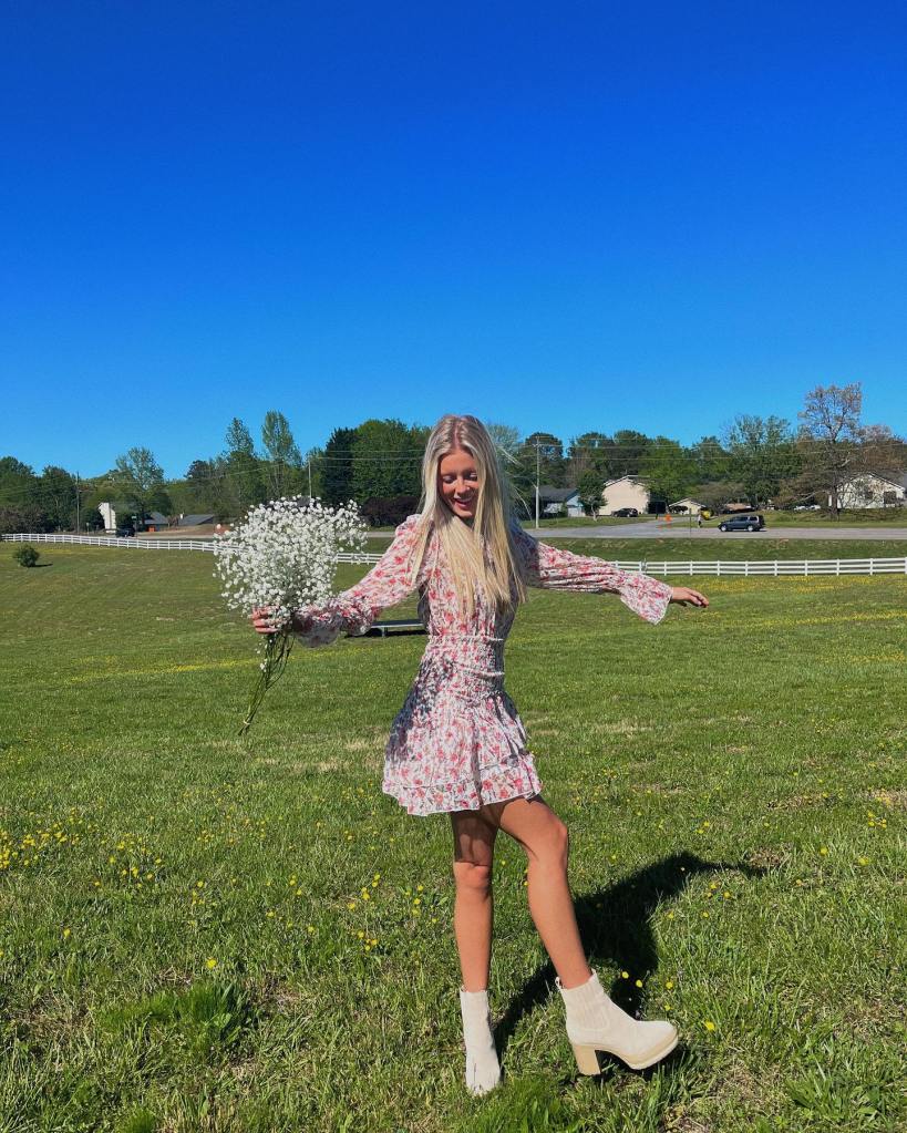 Annabelle Ham in field holding flowers in a pink dress and white boots