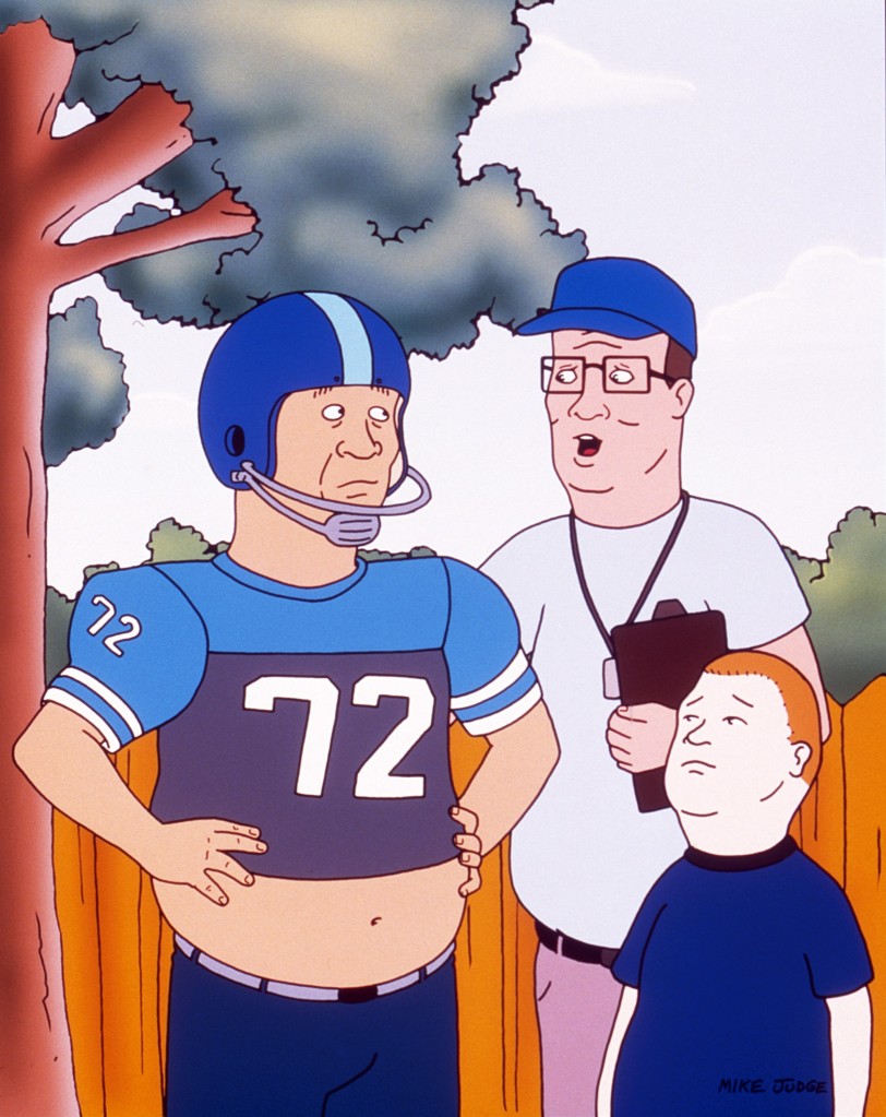 Scene from "King of the Hill." Bill (Stephen Root) is wearing a football helmet, which his bare gut showing. He's talking to Hank (Mike Judge), who's holding a clipboard and wearing a baseball cap and whistle, and Hank's son, Bobby.