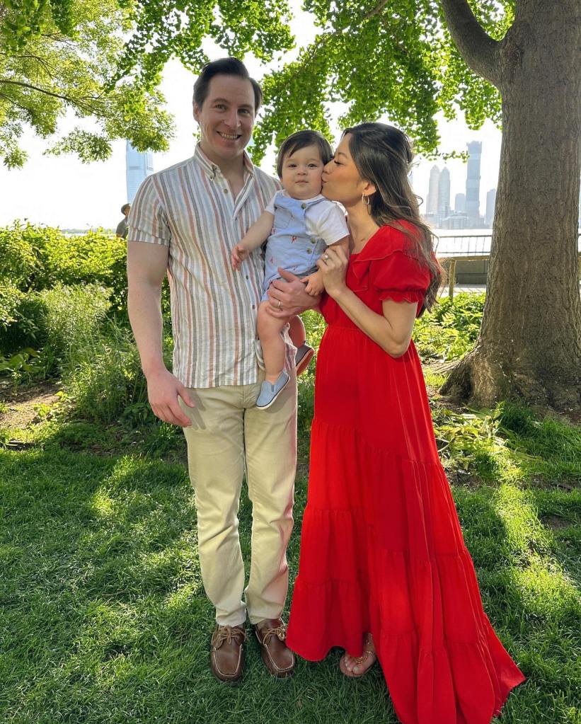 Man in striped shirt and beige pants standing with woman in red dress holding baby boy.
