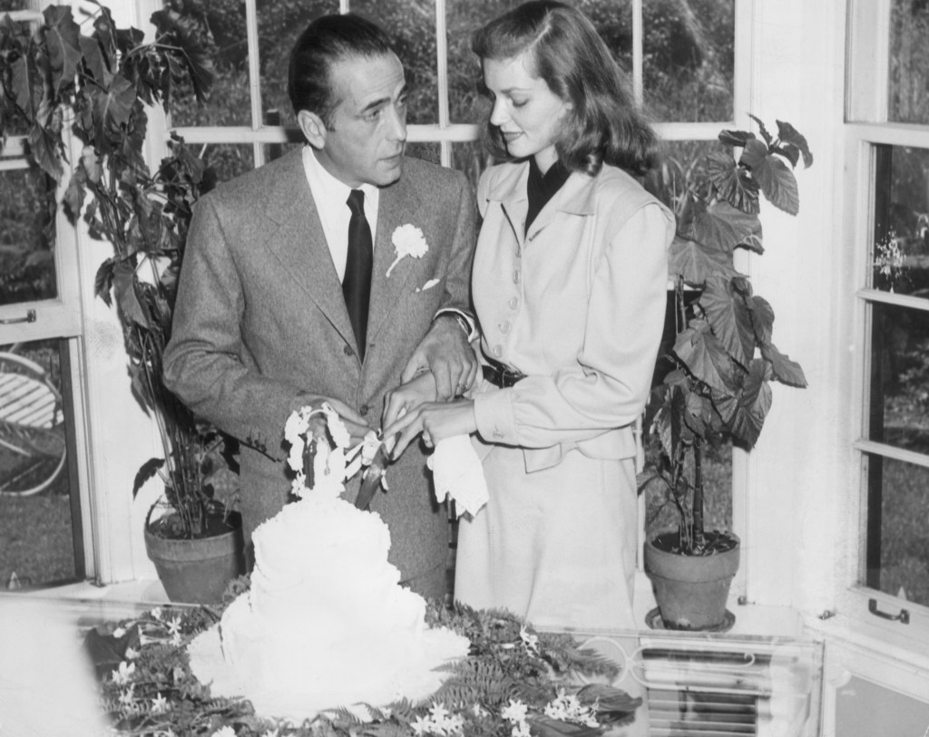Humphrey Bogart and Lauren Bacall cutting a wedding cake.