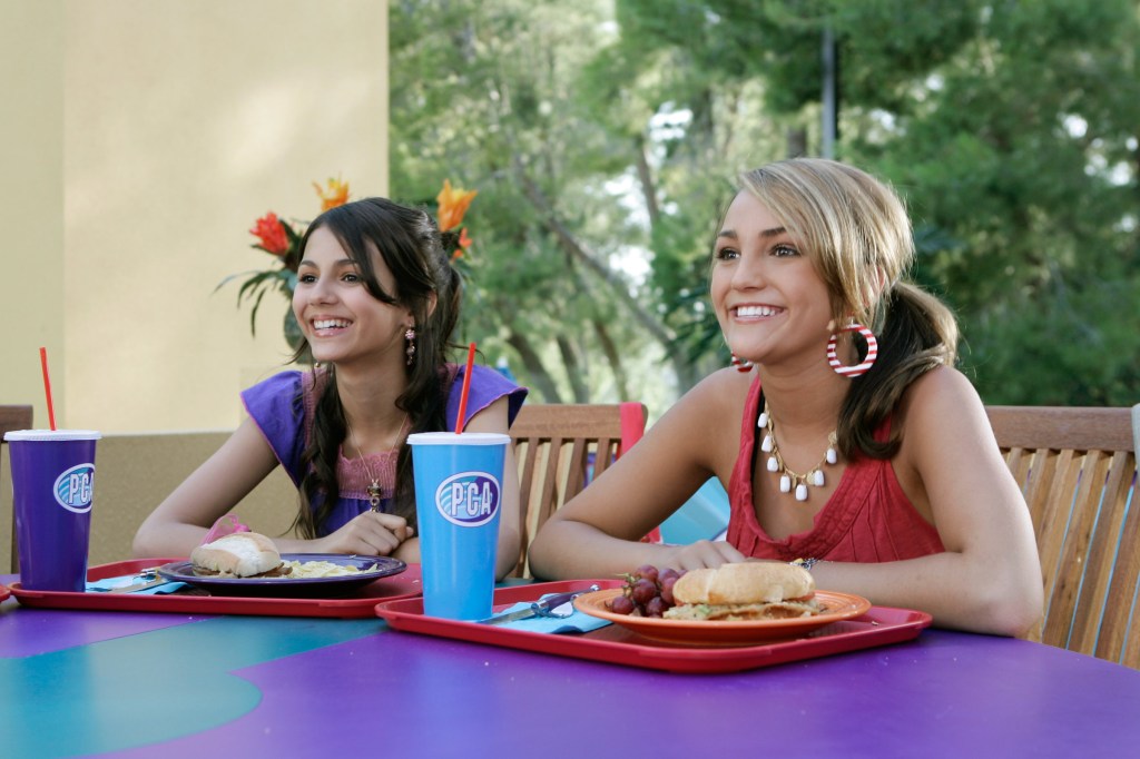 Victoria Jackson and Jamie Lynn Spears in an episode from "Zoey 101" that aired in 2006. They're sitting side-by-side at a school lunch table with trays in front of them. They're both smiling at something while looking straight ahead.