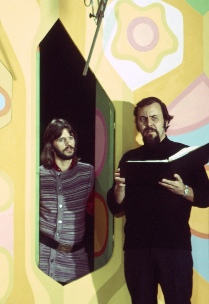 Color photo of George Schlatter and Ringo Starr rehearsing a skit on the set of "Laugh-In." Ringo is looking at George, who's holding a script and is dressed all in black.
