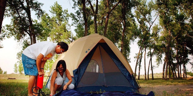 Two people inflating an air mattress outside of a tent 