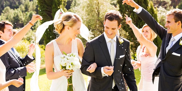 Happy couple walking while guests throwing confetti on them during wedding ceremony.