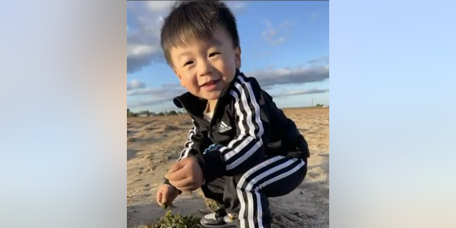 Jasper Wu squats and smiles on the beach