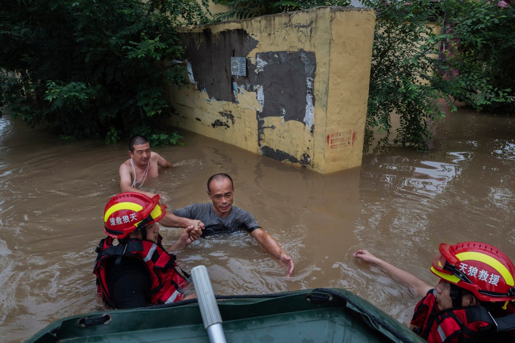 Local residents struggle in deep fast moving water as they make their way towards rescuers to be taken away in a boat in an area inundated with floodwaters on Aug. 3, 2023 near Zhuozhou, Hebei Province south of Beijing, China. 