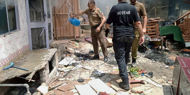 A Pakistani police officer pours water on a burning house