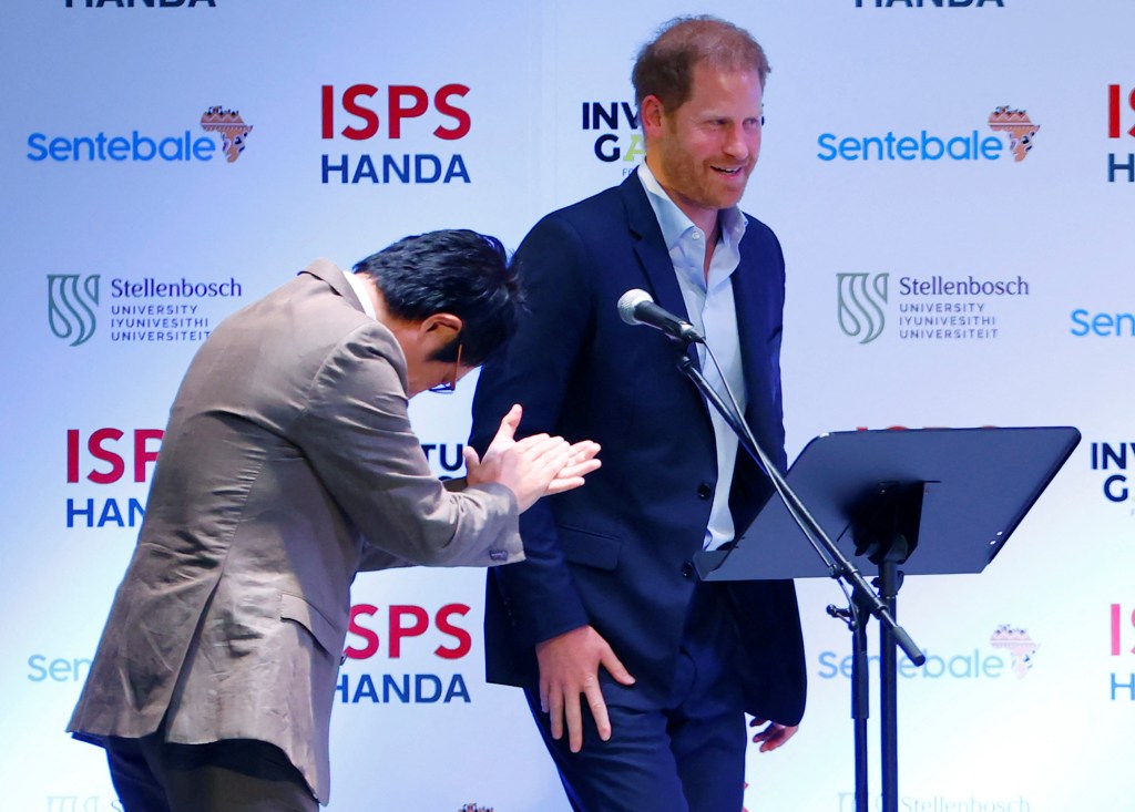 A staff member applauds Prince Harry as he gets on a stage during a summit on the power of sport, community and philanthropy at the ISPS Sports Values Summit-Special Edition in Tokyo, Japan, on Aug. 9, 2023.