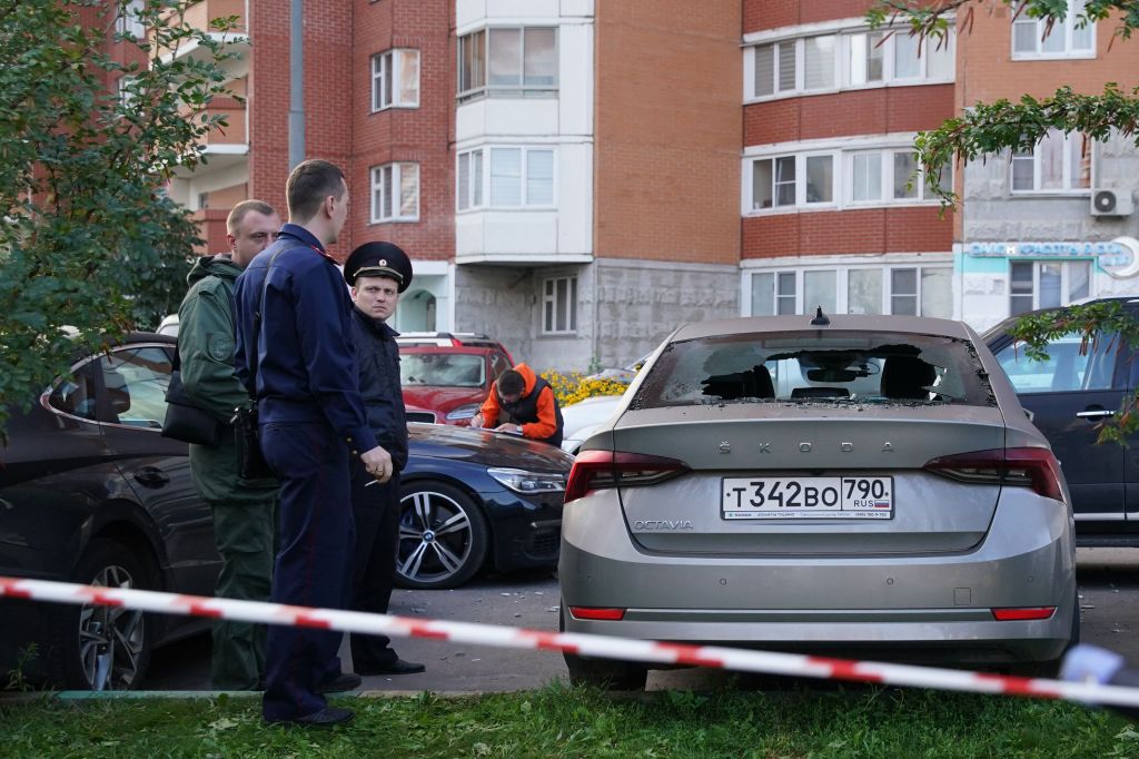 Law enforcement officers stand next to a damaged car following the drone attack in Krasnogorsk, in the Moscow region on Aug. 22, 2023. 