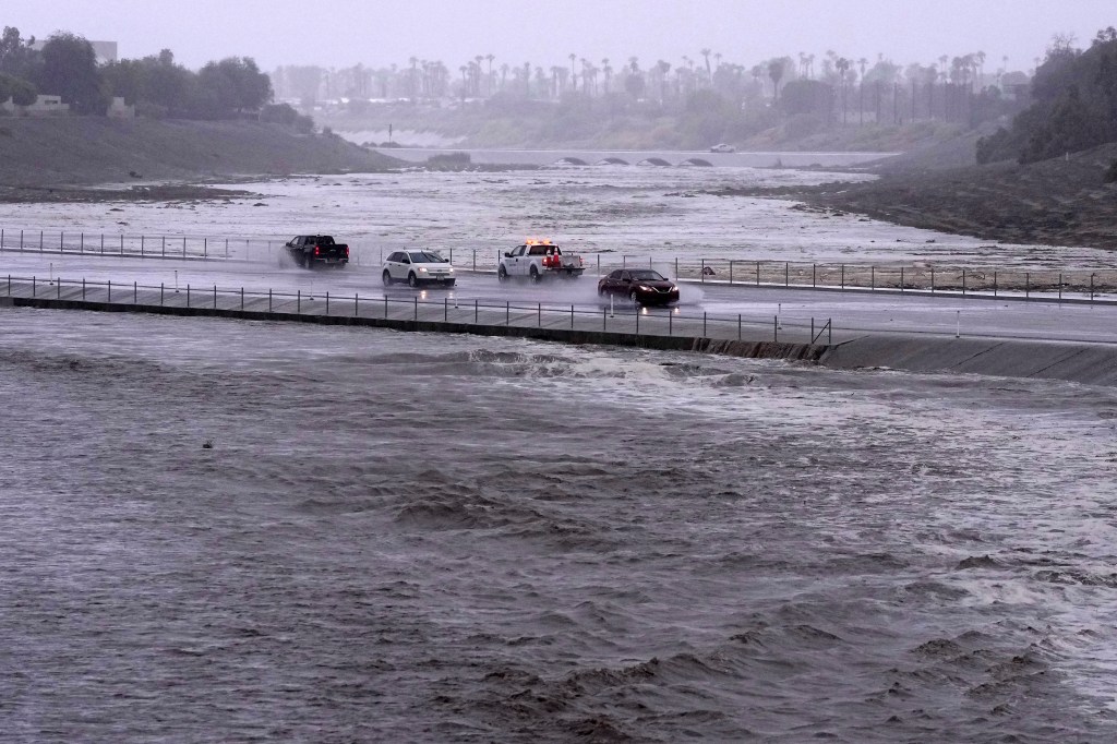 Vehicles cross over a flood control basin that has almost reached the street, on Aug. 20, 2023, in Palm Desert, Calif. 