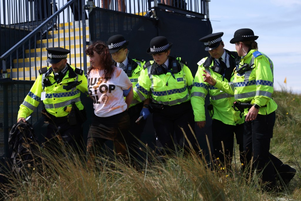 A Just Stop Oil protester is led away by police and security near the 17th hole during the second day of the British Open Golf Championships at the Royal Liverpool Golf Club in Hoylake, England, on July 21, 2023. 