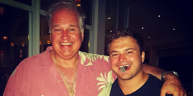 John Daniels smiles with cigar in mouth next to another man