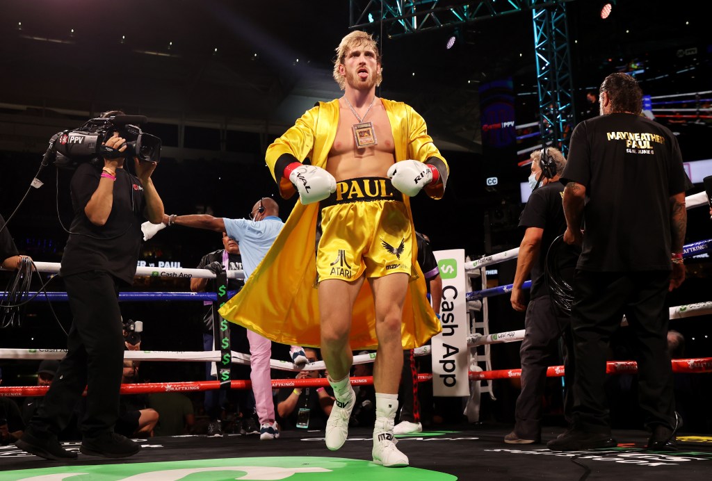 Logan Paul in a yellow robe and boxing shorts and gloves in a boxing ring. 