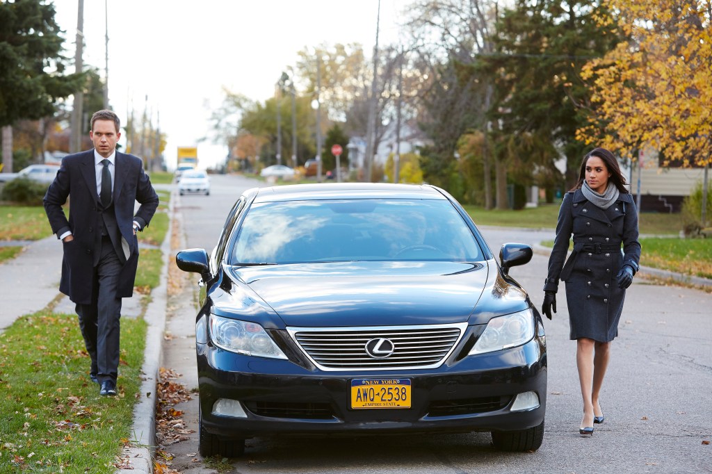 Meghan Markle and Patrick J Adams walking on either side of a car. 