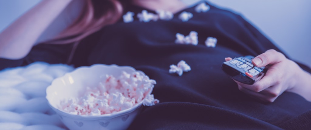 Close-up of a person watching TV with a bowl of popcorn that has been spilled onto their shirt. 