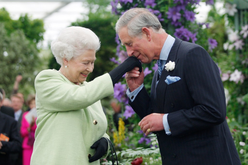 King Charles kissing Queen Elizabeth's hand in a garden. 