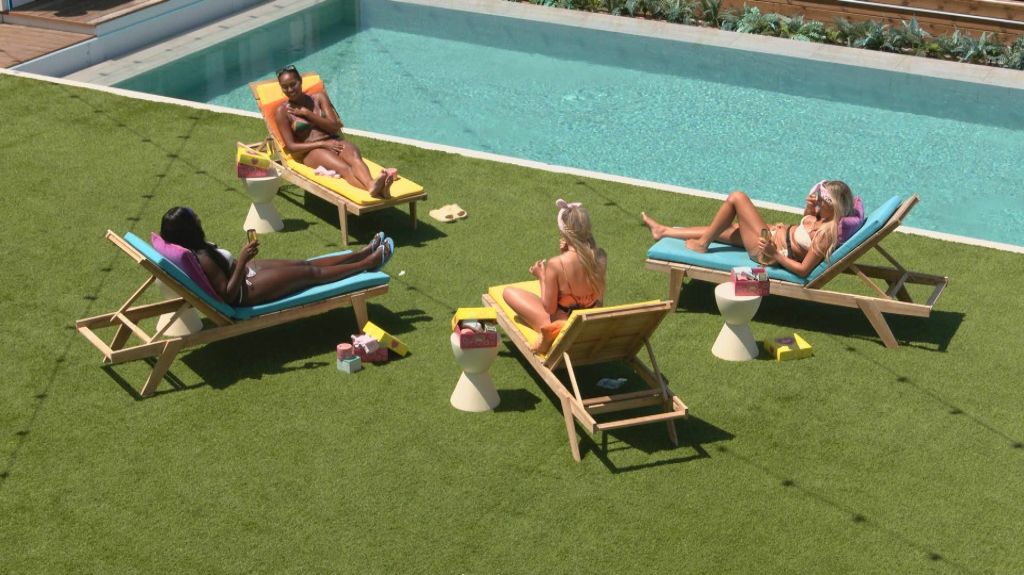 Love Island season 10 contestants sit on lounge chairs.