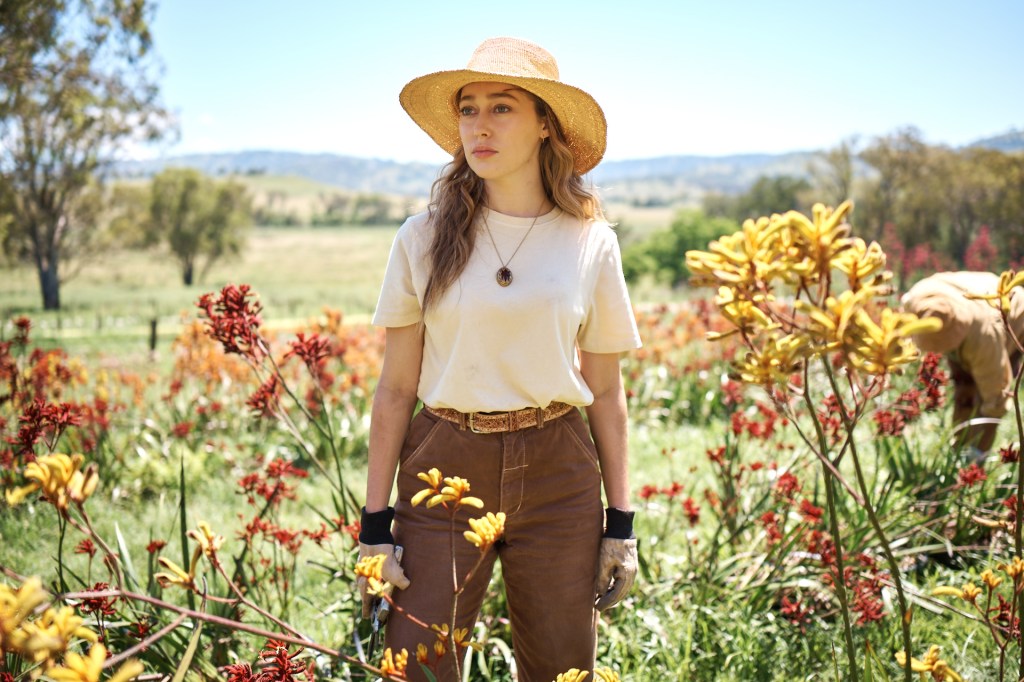 Alycia Debnam-Carey in a flower field wearing a hat. 