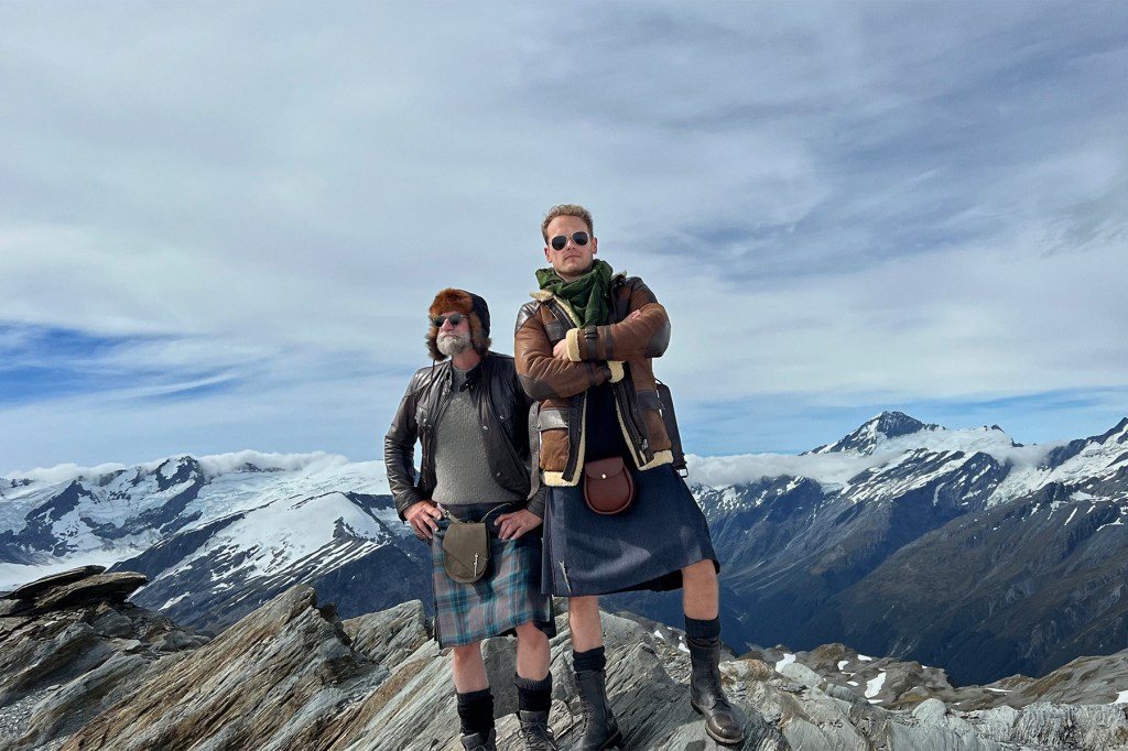 Sam Heughan and Graham McTavish wearing kilts standing on a mountain top. 