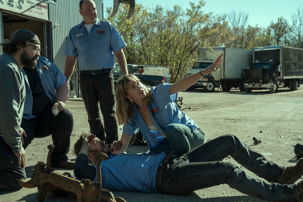 Taylor Kitsch lying on the ground while people crowd around him. 