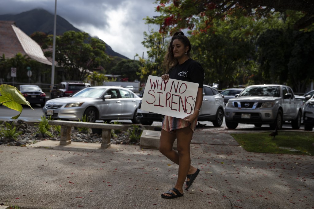 A protester holds a poster reading 'Why no Sirens' as people demonstrate in front the Maui County Building where officials hold a press conference