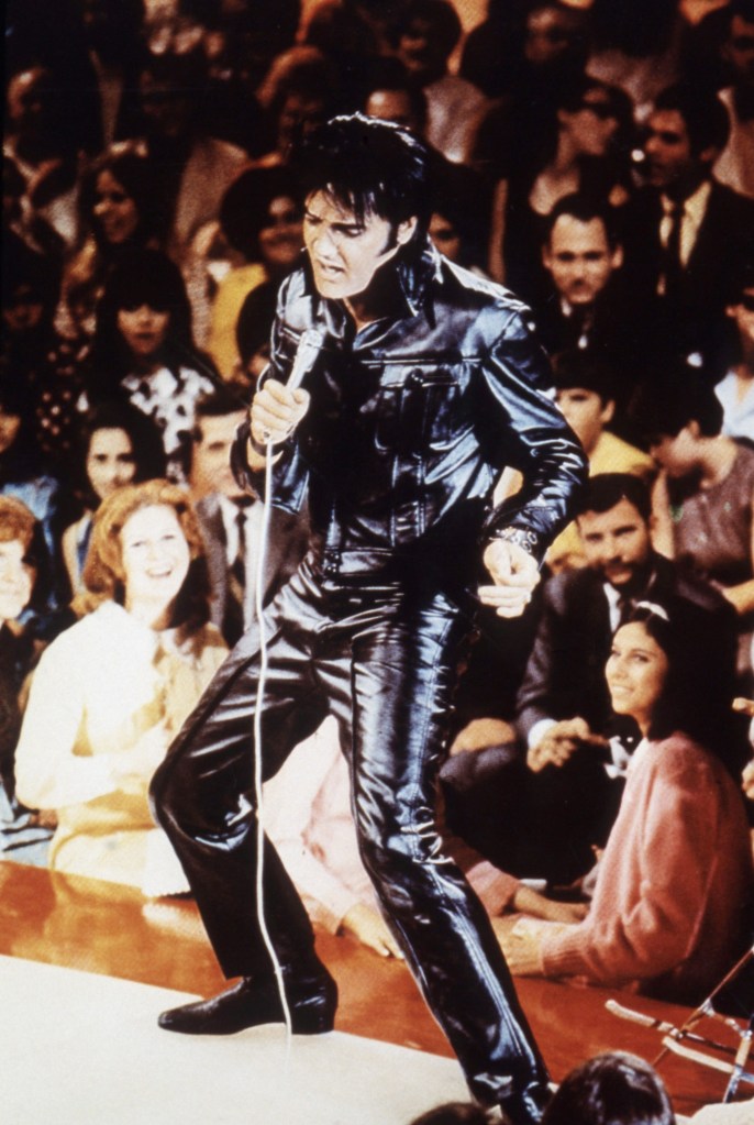 Shot of Elvis from the 1968 NBC special. He's swiveling his hips while holding a microphone and singing. His eyes are shut.