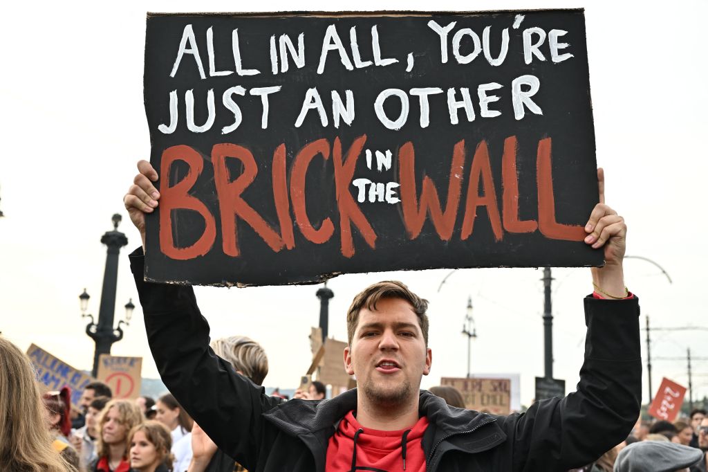 A young man holds up a placard with a quote from Pink Floyd's song "Another Brick in the Wall" as students, teachers and sympathizer block the traffic on Margit Bridge to protest against the government's education policy in Budapest, on October 5, 2022, the International Teachers' Day. - People took to the streets in the Hungarian capital on Wednesday to demand better living, working and financial conditions for teaching staff on the International Teachers' Day. (Photo by Attila KISBENEDEK / AFP) (Photo by ATTILA KISBENEDEK/AFP via Getty Images)