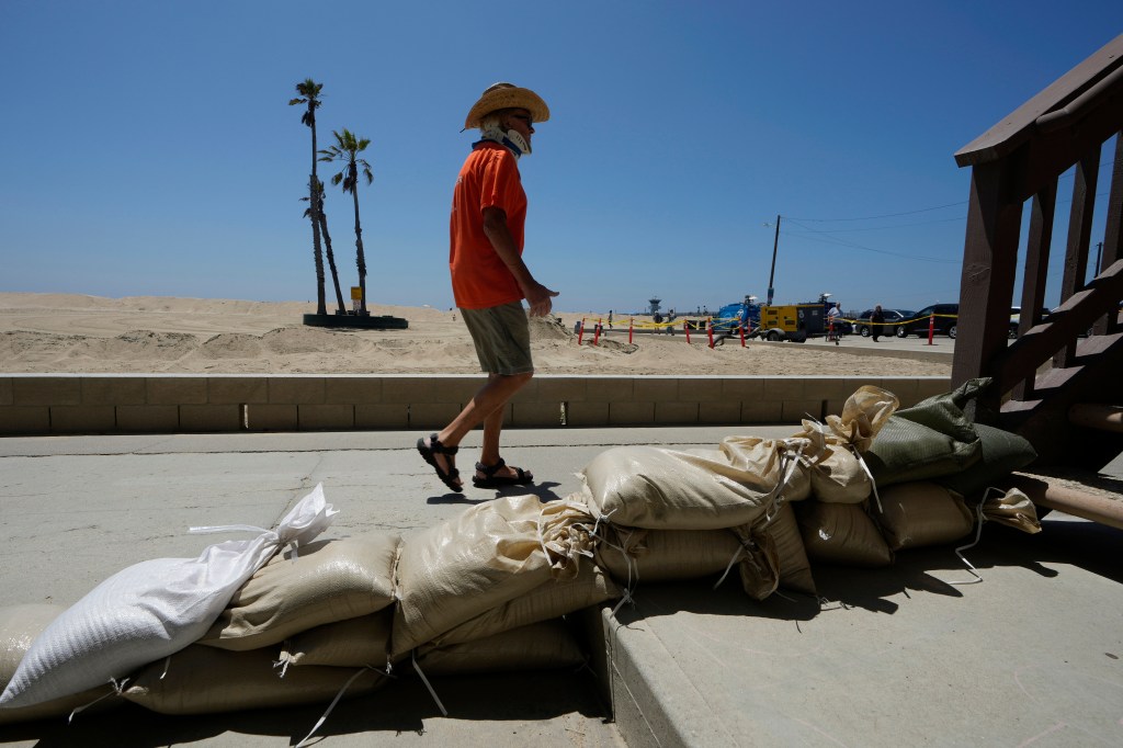 California cities are prepping for Hurricane Hilary, which will become a superstorm, and is expected to bring catastrophic flooding. A man walks past sandbags near the beach in Seal Beach, California.