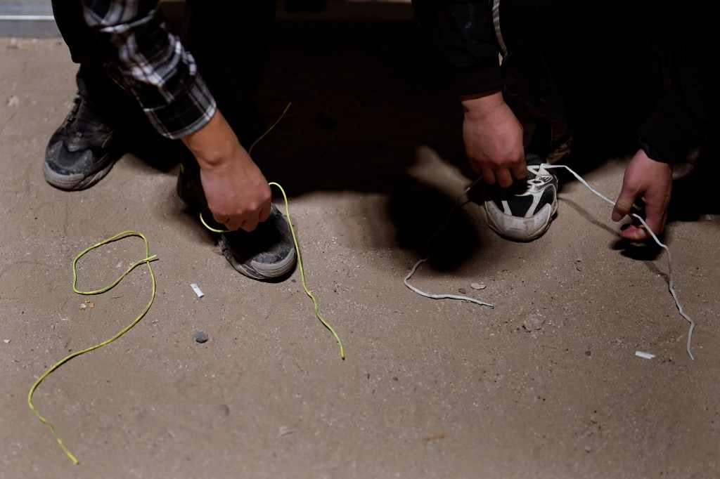 Two men remove their shoelaces as they wait to apply for asylum after crossing the border.