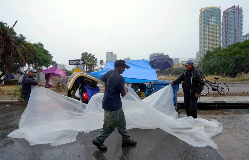 Homeless people carrying a tarp to shield themselves from rain brought in by Tropical Storm Hilary in San Diego.