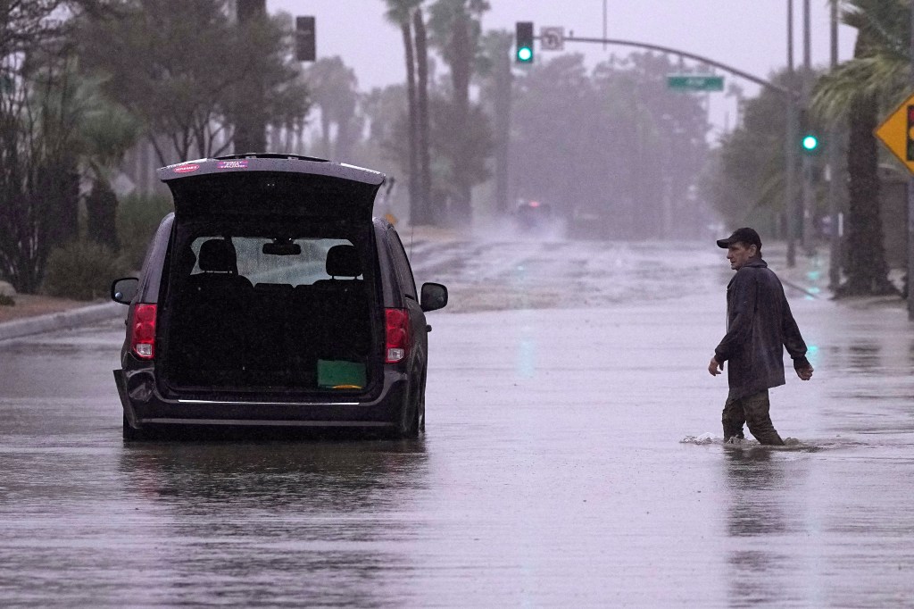 A motorist walking to a stranded car in a flooded Palm Desert street.