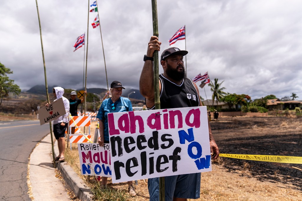 Dustin Pilialoha stands with a sign while waiting for the arrival of President Joe Biden outside the Lahaina Civic Center.