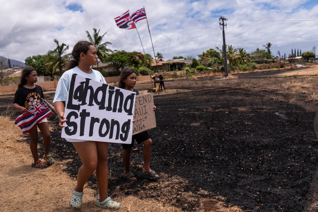 Children hold signs and a Hawaiian flag while waiting for the arrival of President Joe Biden on Monday.