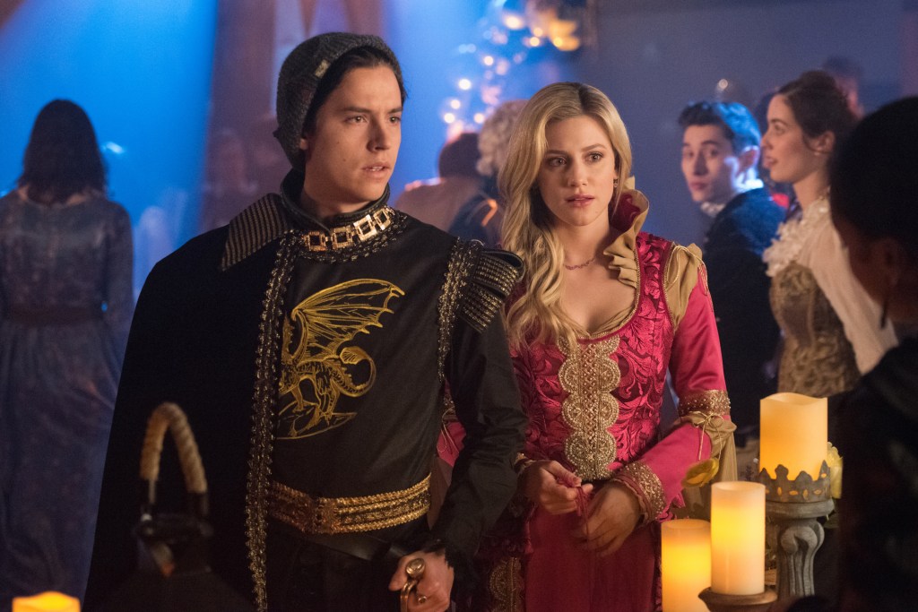 Cole Sprouse as Jughead and Lili Reinhart as Betty wearing medieval outfits looking solemn. 