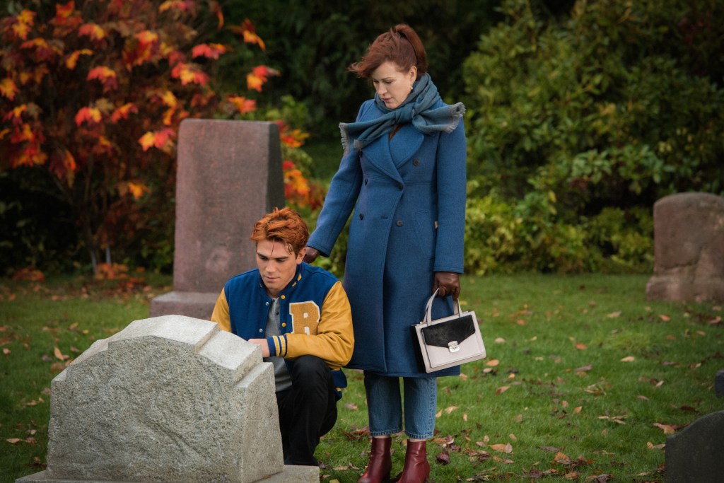 KJ Apa as Archie and Molly Ringwald as Mary Andrews crouching in front of a grave. 